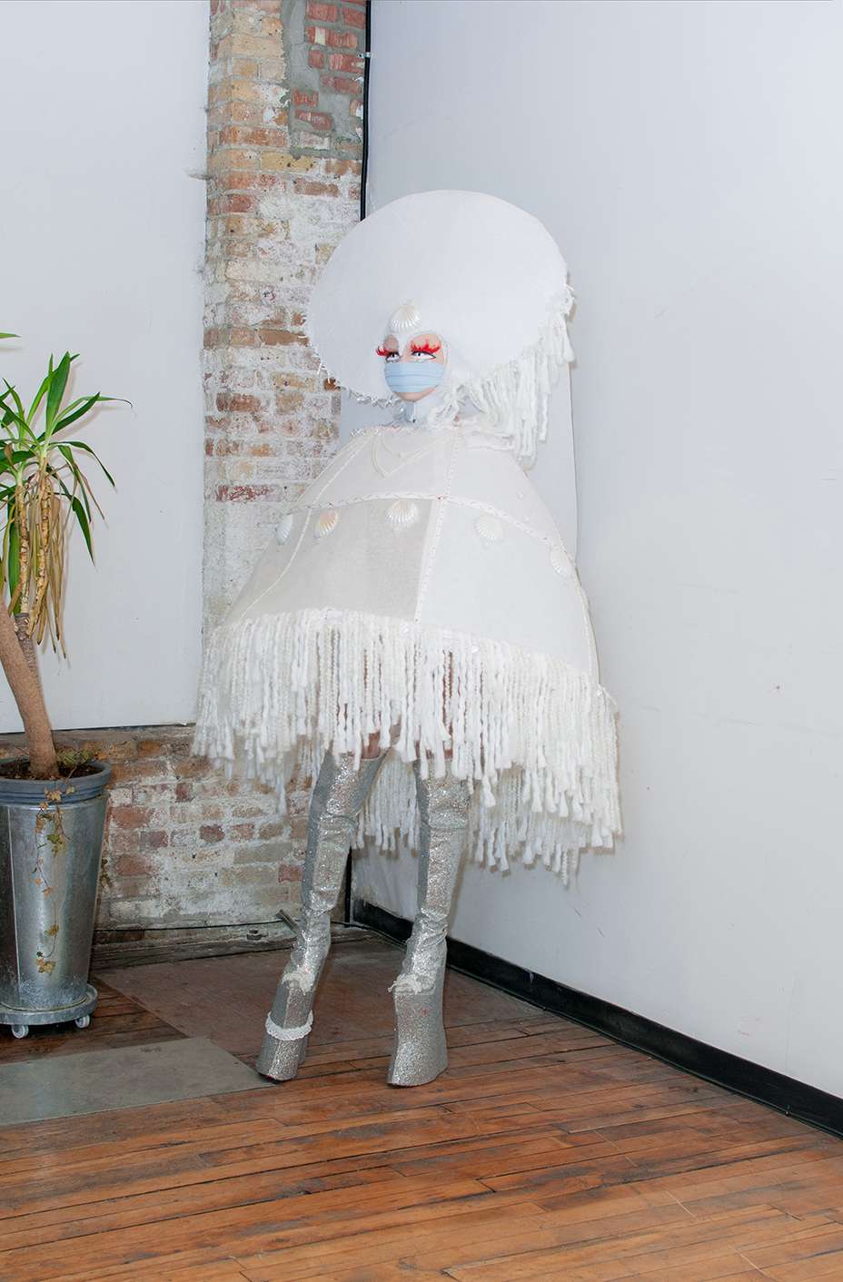 Full body shot of Bon Bon in a large abstract white ourfit against a white wall